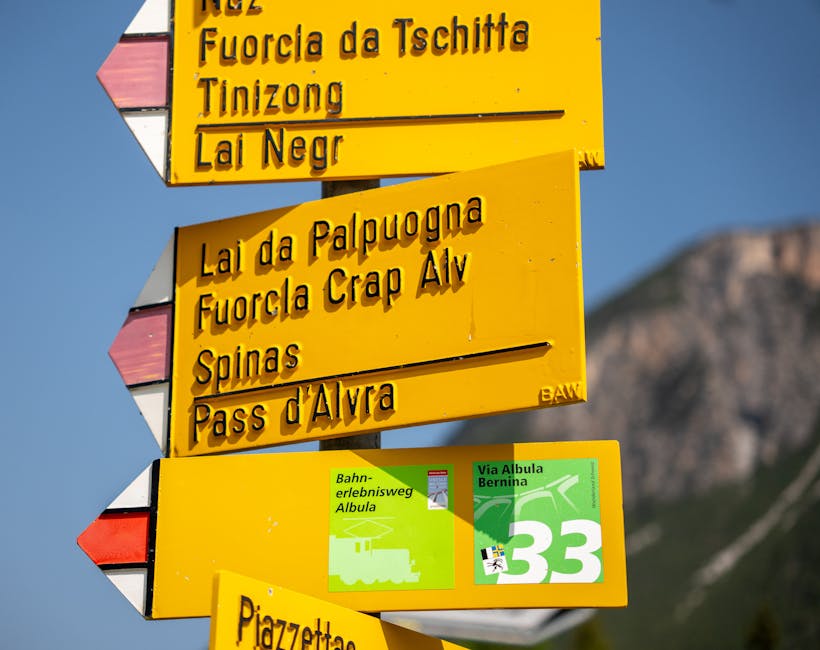 Close-up of a yellow trail sign in La Punt Chamues-ch, Switzerland, with mountains in the background.
