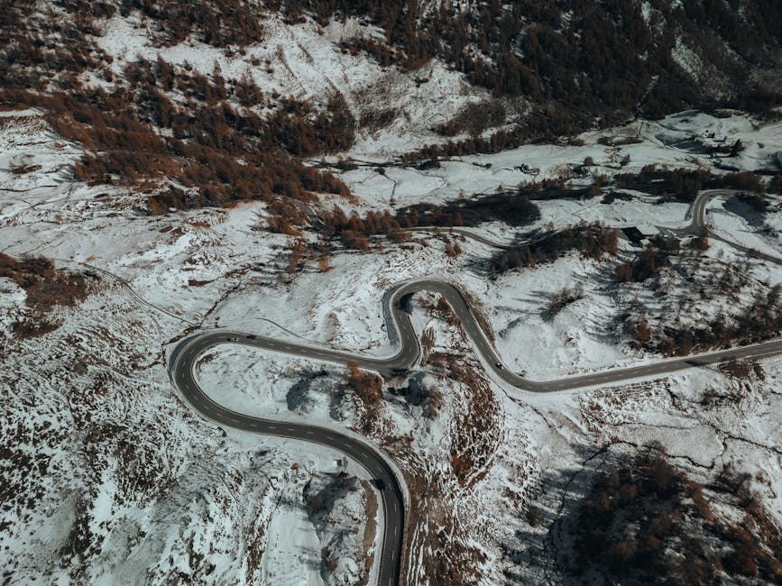 Discover the beauty of a winding road through snowy mountain terrain, captured from above.
